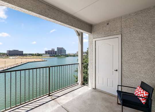 A balcony with a white door and a black chair with a red and white pillow.