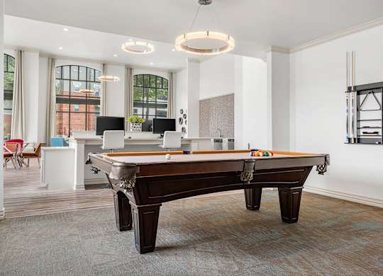 A pool table is in the middle of a room with a white ceiling and a window.