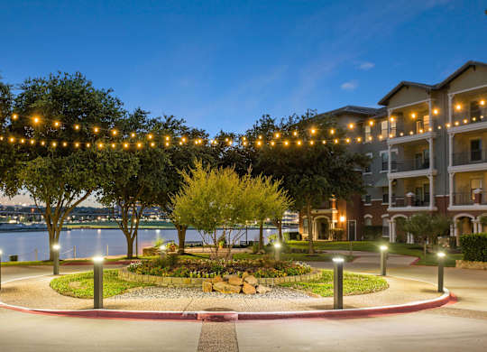A beautifully lit garden in front of apartment buildings at dusk.