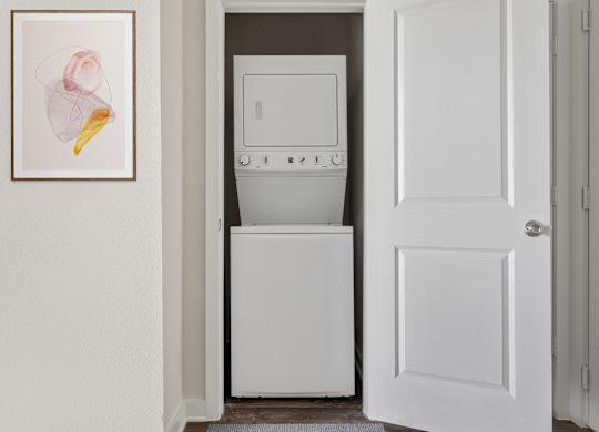 A white dishwasher is in a narrow space between a white door and a white wall.
