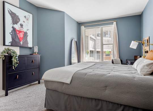 A bedroom with a large bed, a dresser, and a window with blinds.