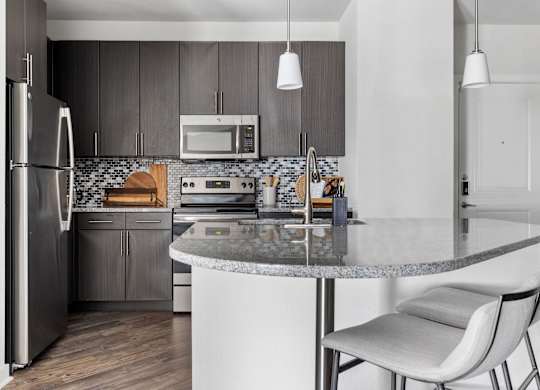 A modern kitchen with a refrigerator, microwave, oven, and a marble countertop.