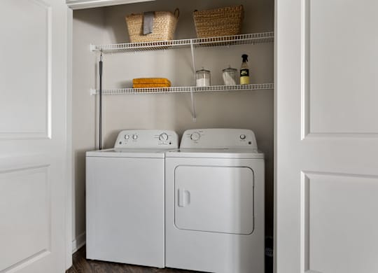 A white laundry cabinet with two washing machines and a shelf above it.