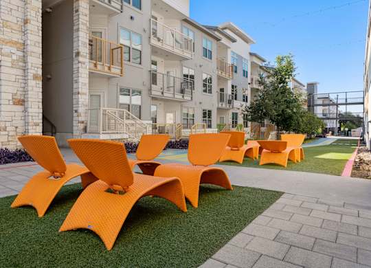 A set of orange chairs are arranged on a lawn in front of apartment buildings.
