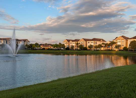 A fountain in the middle of a lake with houses in the background.