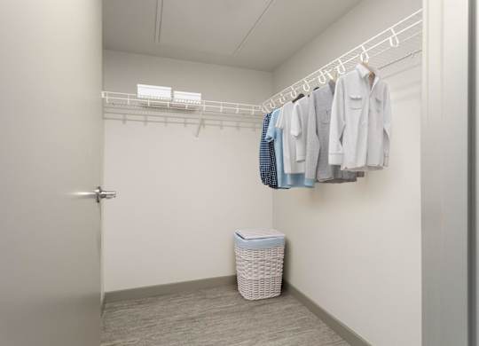 A white closet with clothes hanging and a basket on the floor.