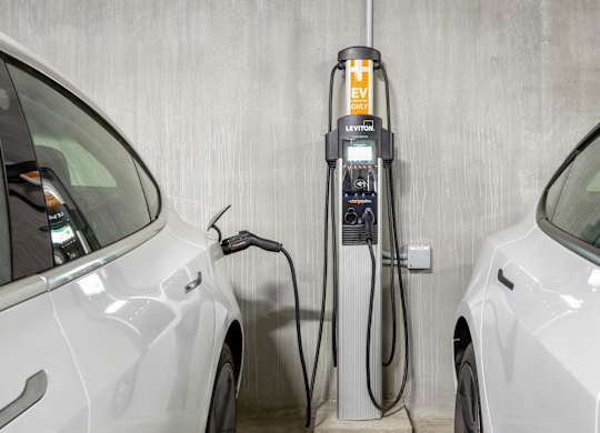A white car is charging at a Leviton electric vehicle charging station.