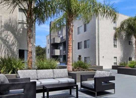 A patio with furniture and palm trees in front of a building.