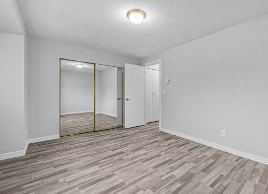 A room with a wooden floor and a white wall with a mirror on the wall.