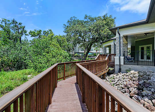 A wooden deck leads to a house with a stone wall.