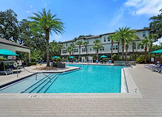 A large swimming pool surrounded by a brick patio and palm trees.
