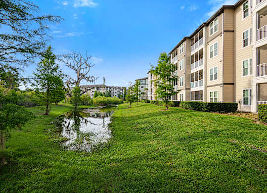 A pond in a grassy area in front of apartment buildings.