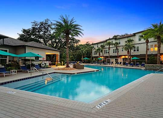 A pool surrounded by palm trees and lounge chairs.