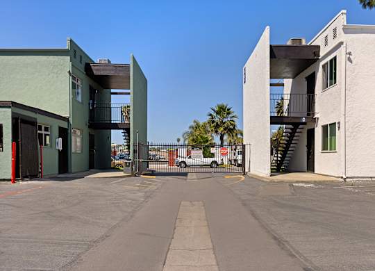 A parking lot with a green building on the left and a white building on the right.