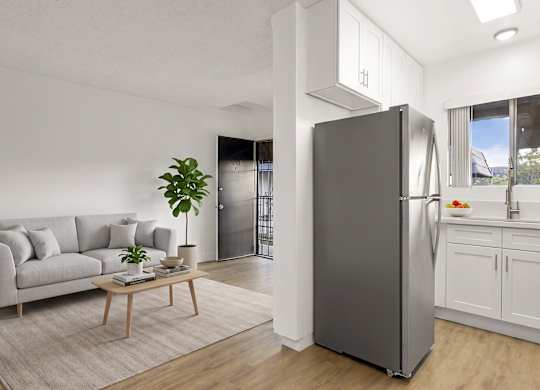 A modern kitchen with a grey refrigerator and a grey sofa with a wooden coffee table in front of it.