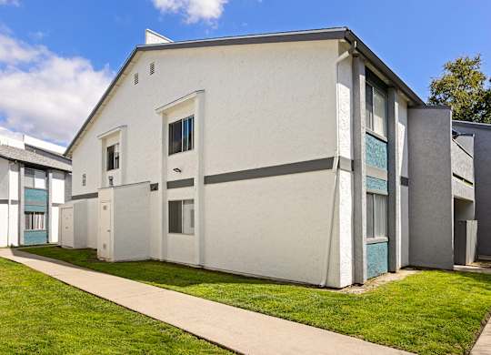 A white building with a grey roof and a green lawn in front.