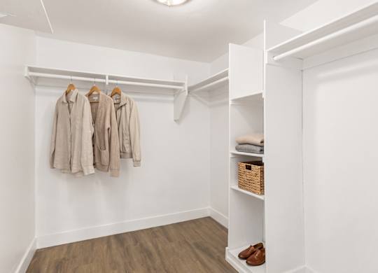 A white closet with a coat hanging on a rod and a basket of shoes on the floor.