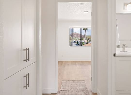 A white doorway leads to a bathroom with a sink and a window.