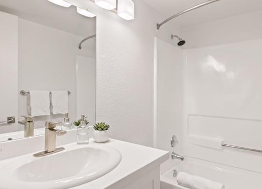 A white bathroom with a sink, mirror, and shower.