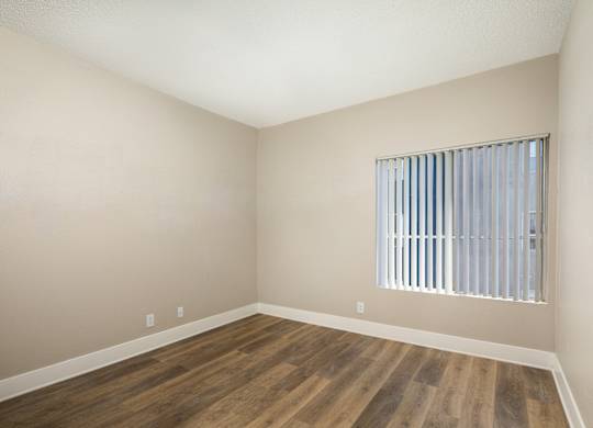 A room with wooden flooring and a window with blinds.