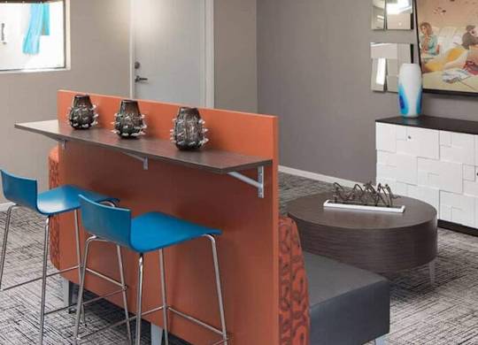 A modern kitchen with orange bar stools and a grey countertop.