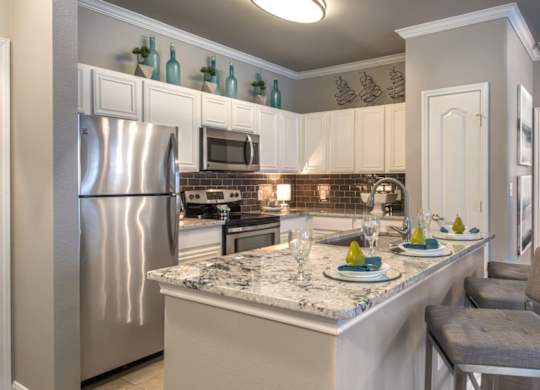A kitchen with a marble countertop and a stainless steel refrigerator.