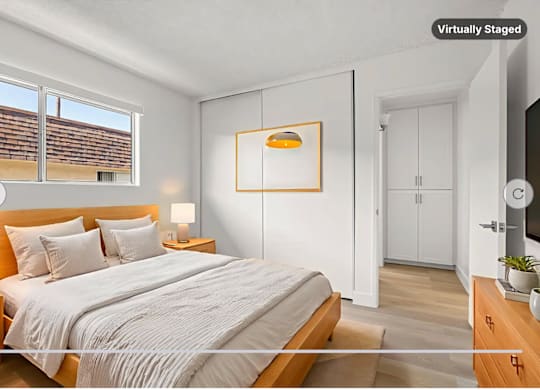 A bedroom with a large bed, a nightstand with a lamp, and a TV on the wall.