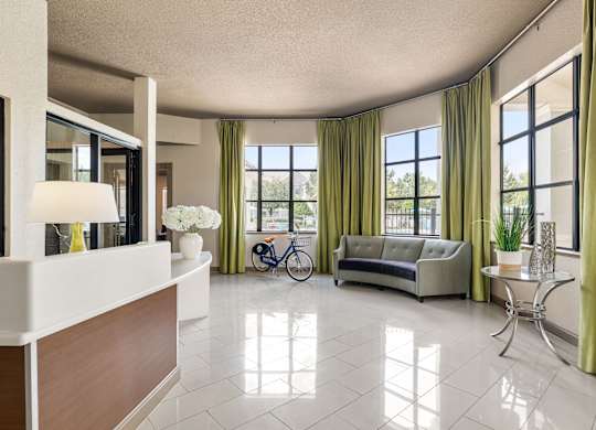 A well-lit, spacious living room with a white reception desk and a bicycle in the background.