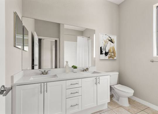 A white bathroom with a double sink and a toilet.
