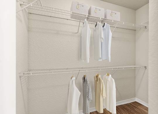 A white closet with clothes hanging on hangers.