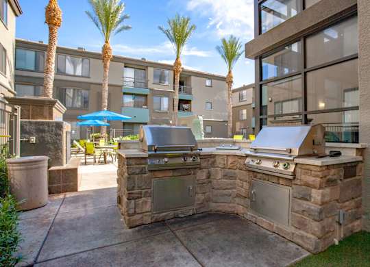 A stone BBQ area in a courtyard with a building in the background.