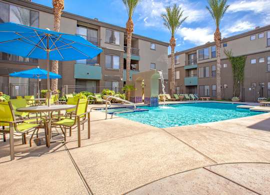 A pool surrounded by chairs and umbrellas in a courtyard.