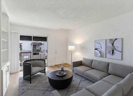 A living room with a grey couch, a black chair, and a table with a lamp on it.