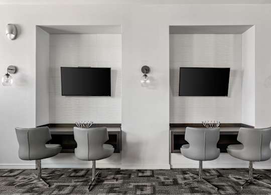 Two chairs are placed in front of two TVs on a wall.