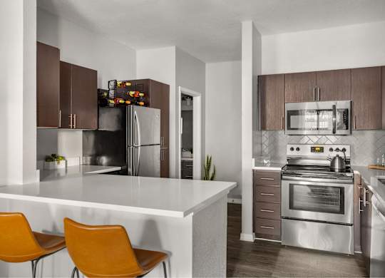 A modern kitchen with a white island and orange chairs.