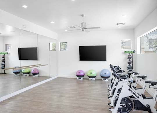 A gym with a row of exercise bikes and two television screens on the wall.