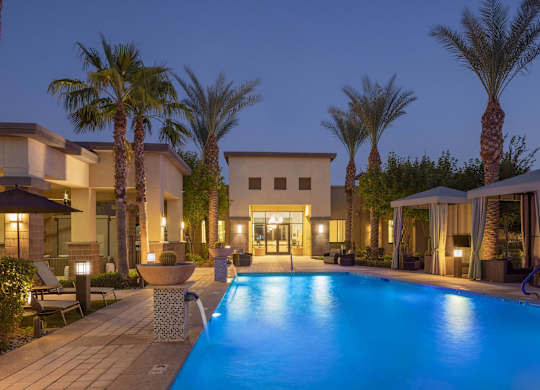 A pool surrounded by palm trees and a building in the background.