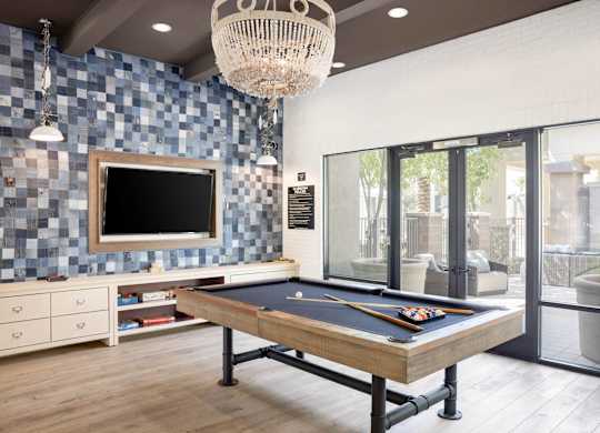 A pool table is in the middle of a room with a tv and a chandelier.