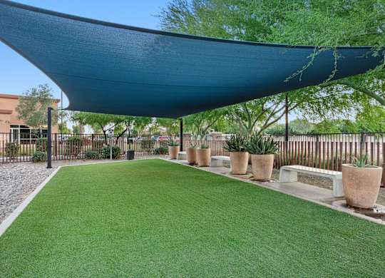 A patio with a blue shade sail and artificial grass.