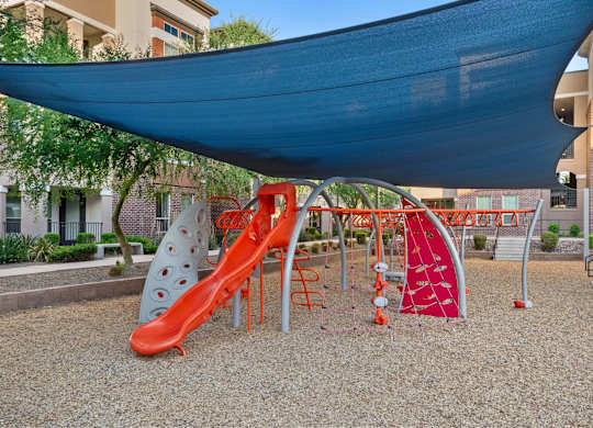 A playground with a red slide and a blue canopy.