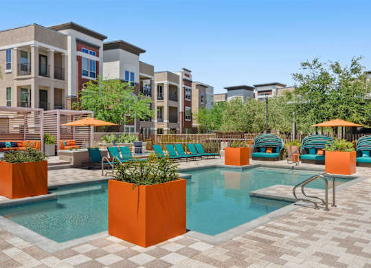A pool surrounded by orange planters and chairs.