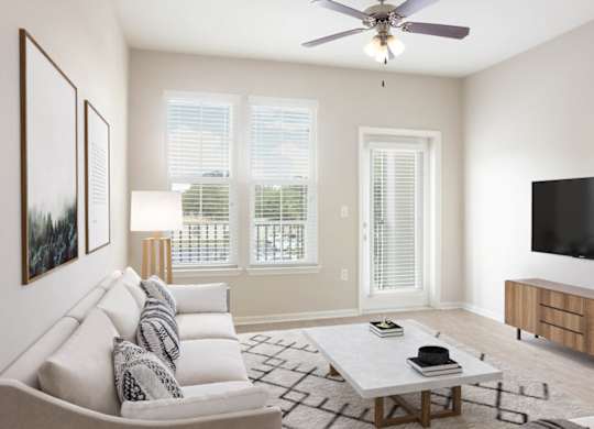 A living room with a grey couch, a coffee table, a flat screen TV, and a ceiling fan.