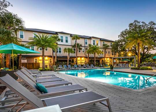 A pool surrounded by lounge chairs and umbrellas in front of a building.