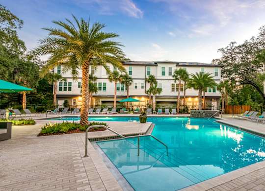 A swimming pool surrounded by lounge chairs and palm trees in front of a hotel.