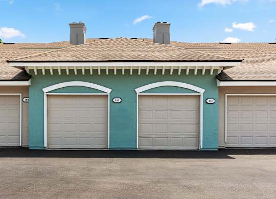 A two-car garage with white doors is attached to a house with a brown roof.