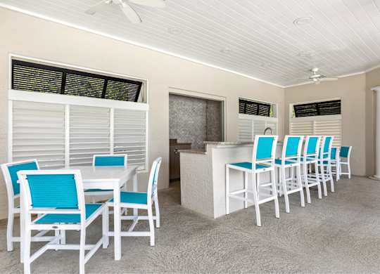A white table with blue chairs is in a room with a ceiling fan.