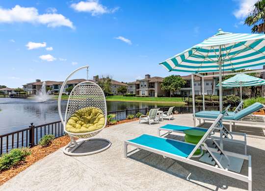 A sunny day at the poolside with a chair, table, and umbrella.