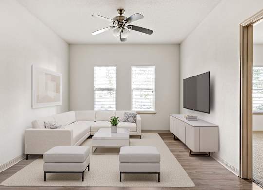 A living room with a white sofa set, a television, and a ceiling fan.