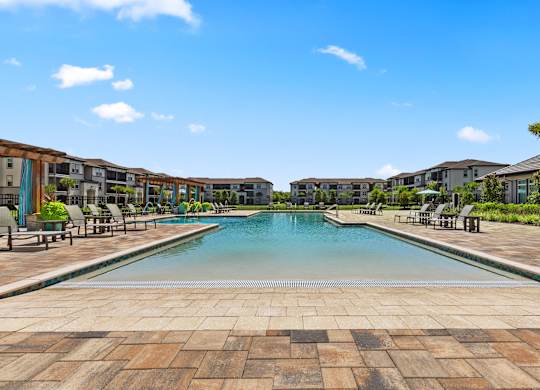 A large swimming pool surrounded by a brick patio and lounge chairs.