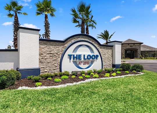 A sign for The Loop at 2700 with a blue sky and palm trees in the background.